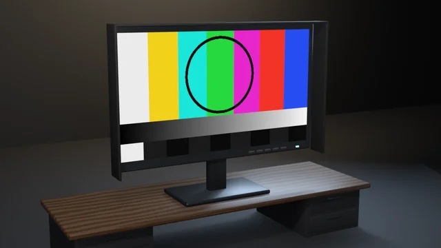A hooded broadcast reference monitor on a walnut desk showing a colour-bar test card with a black circle, a greyscale ramp and a PLUGE row.